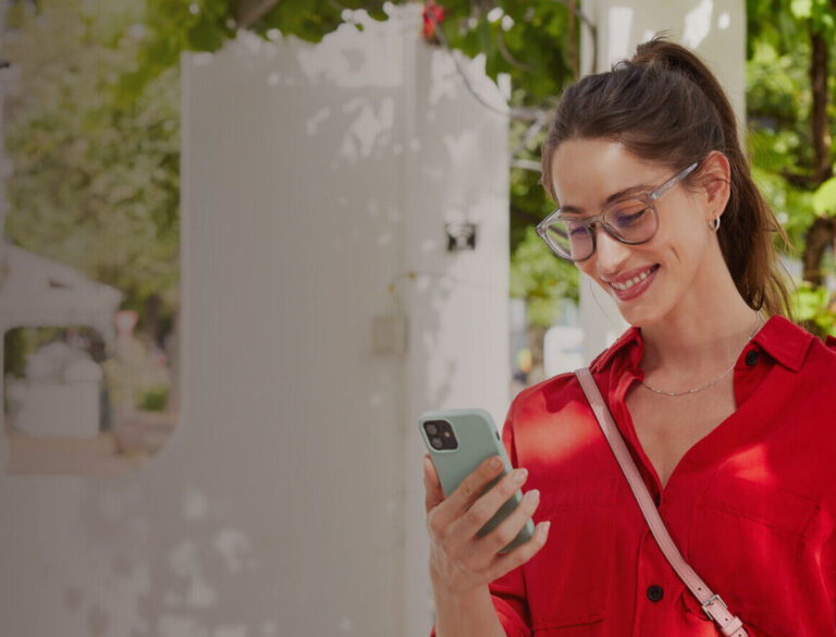 A woman in a red top smiling at her phone standing outside tracking her dad Ireland parcel