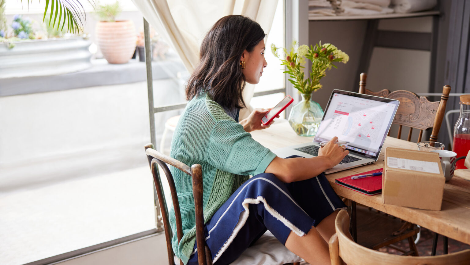 DPD Ireland customer sitting at kitchen table on her phone and laptop tracking her parcel.